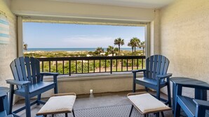 Un balcon avec deux fauteuils Adirondack bleus, une petite table et une vue sur la plage et l’océan.