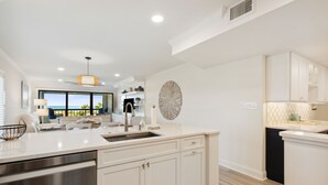 Une cuisine moderne avec des meubles blancs, un grand îlot central doté d’un évier et une vue sur l’extérieur.