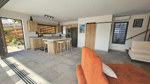 A modern kitchen with wooden cabinets, a central island with bar stools, and a dining area. - Villa Eclats Panoramiques (Saint-Pierre)