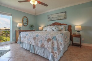 A bedroom with a bed, two bedside tables, a ceiling fan, a window with a view, and a painting on the wall. - LOVELY WATERFRONT BAY VILLAGE 2B/2B CONDO! WALK TO BEACH! (Fort Myers Beach)