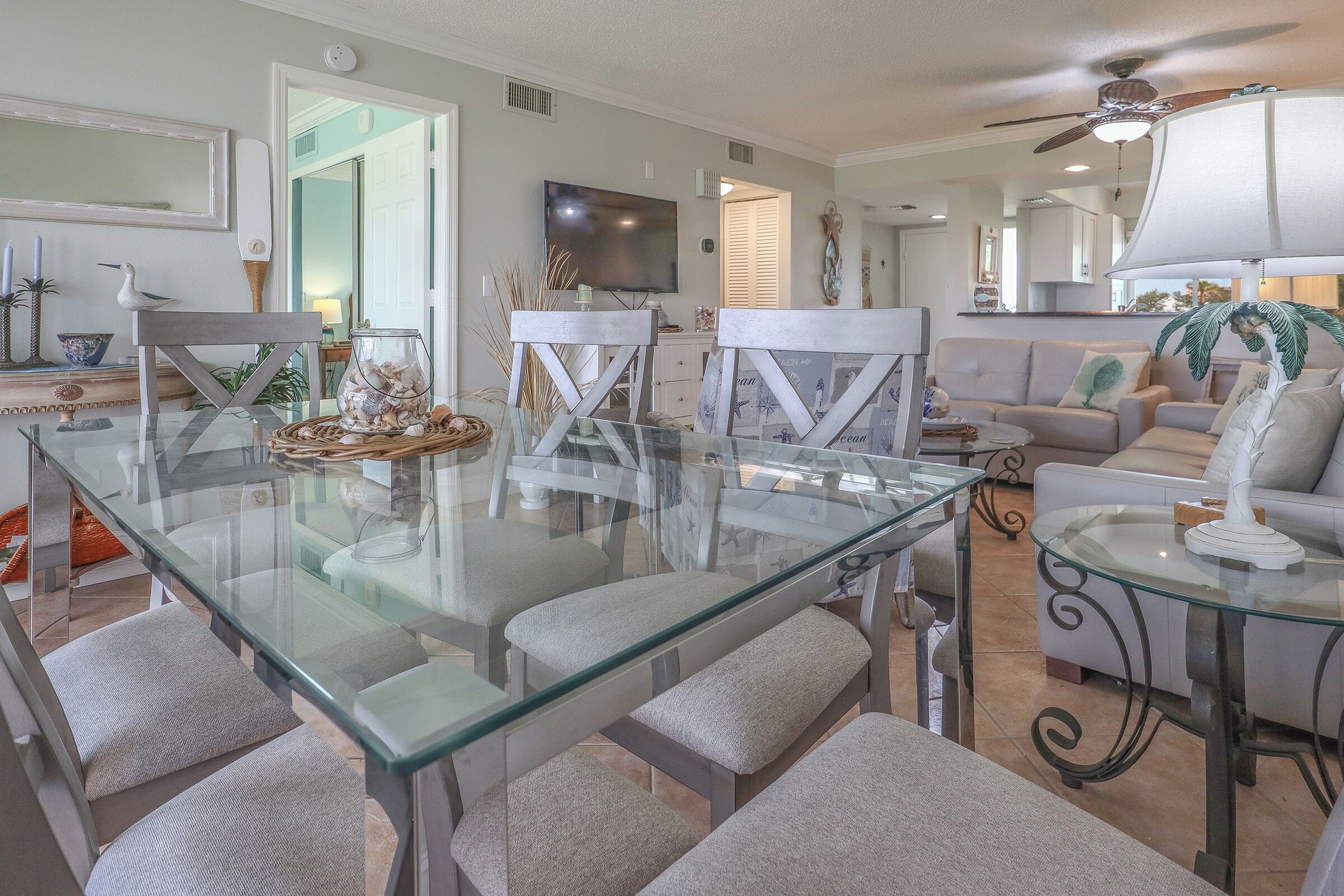 A modern living room with a glass dining table, comfortable seating, a flat-screen TV, and a ceiling fan.