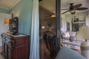 Una sala de estar con televisión sobre un mueble de madera, un sofá, un sillón y un ventilador de techo.