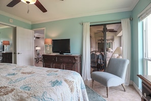 Un dormitorio con cama, una silla, televisor y cómoda.