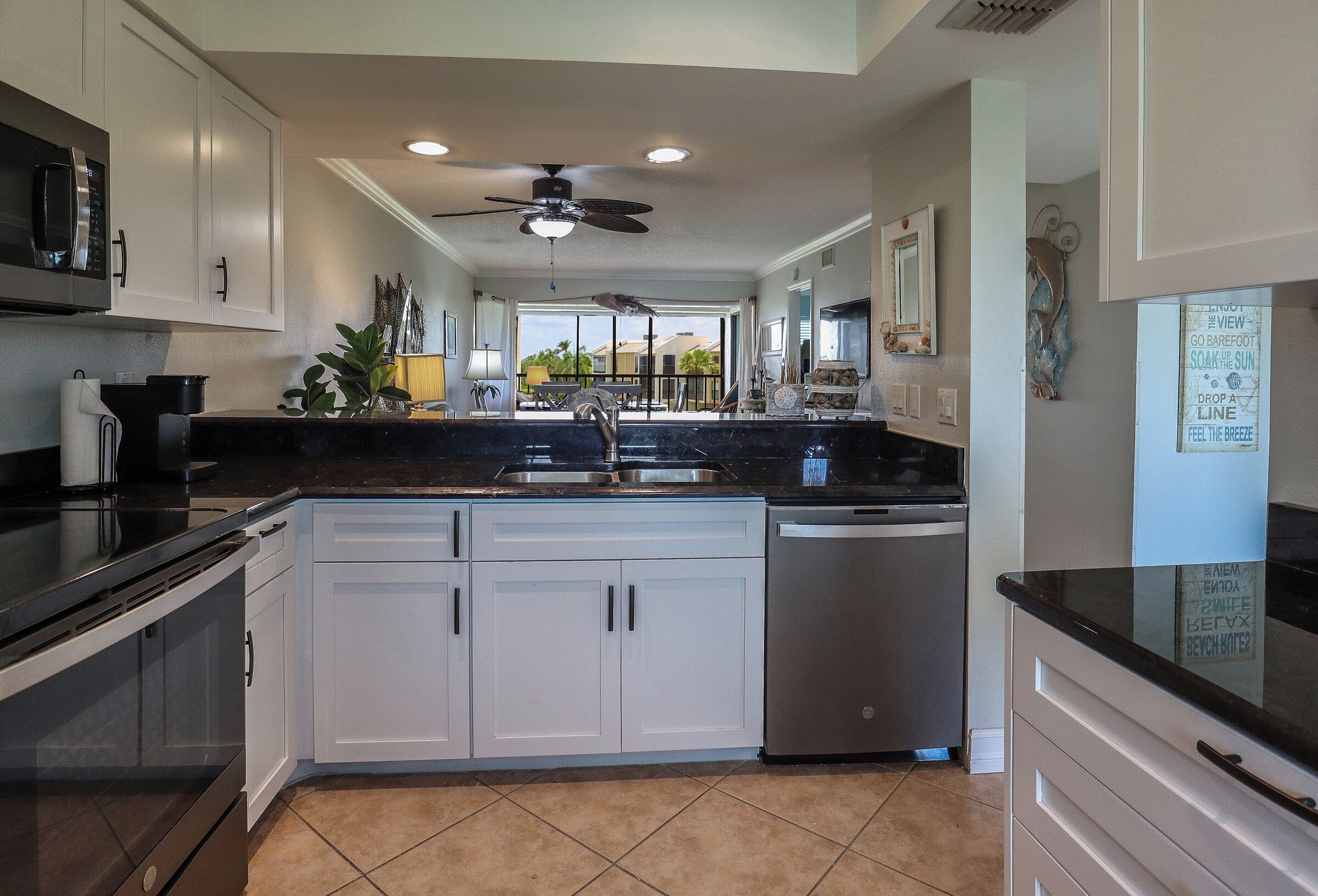 A kitchen with white cabinets, a black countertop, a dishwasher, and a ceiling fan.
