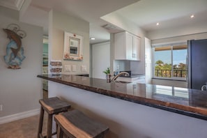 A modern kitchen with a central island, white cabinetry, and a view to the outside. - LOVELY WATERFRONT BAY VILLAGE 2B/2B CONDO! WALK TO BEACH! (Fort Myers Beach)
