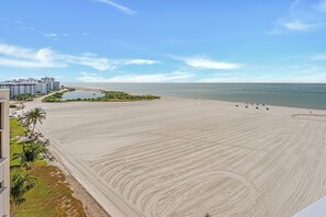 A beach with a clear view of the ocean, a sandy area, and a few buildings in the background.