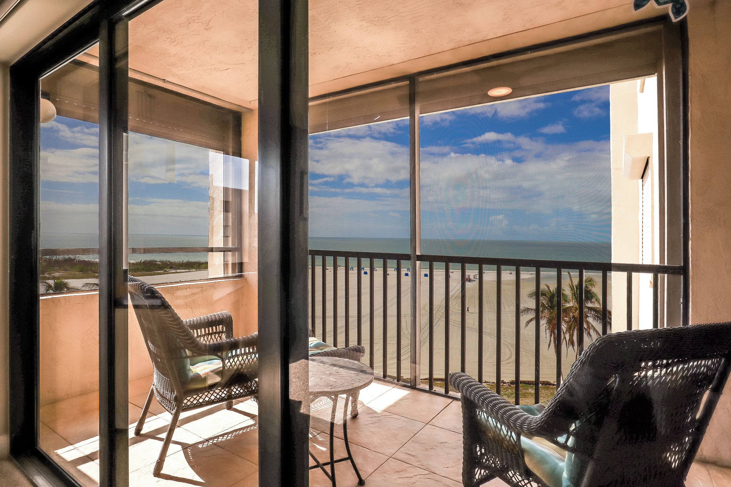 Un balcon avec vue sur la plage, des meubles en osier et une petite table.