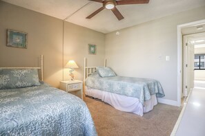 A bedroom with two beds, a ceiling fan, and a nightstand with a lamp.
