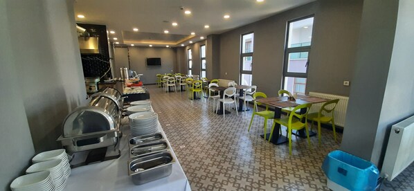 A dining area with tables and chairs, a buffet line with dishes and utensils, and a television on the wall.