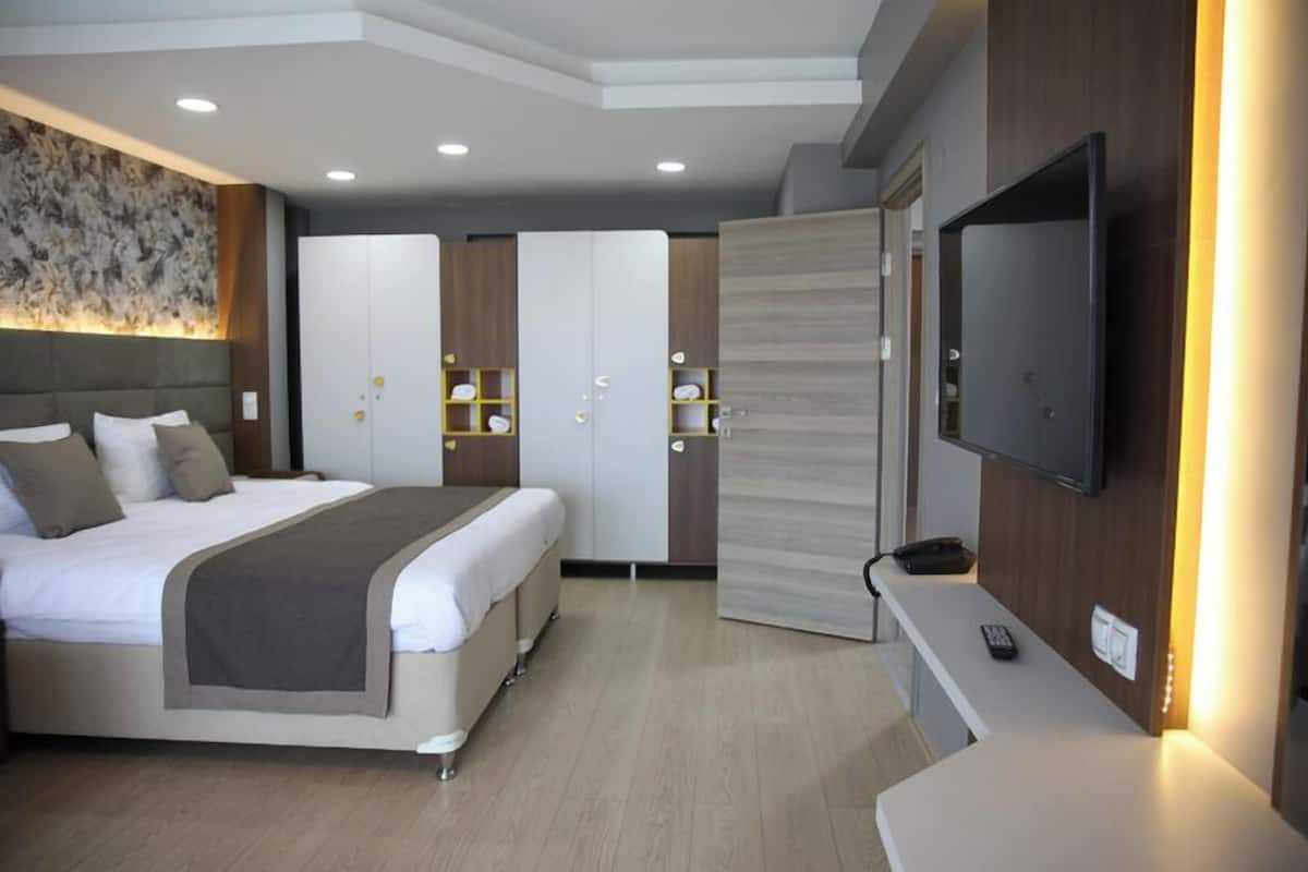 Quarto de hotel moderno com cama grande, televisão presa à parede e mesa com controle remoto.