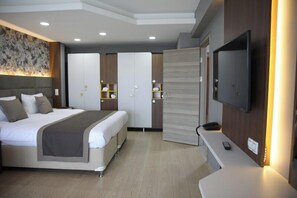 A modern hotel room with a large bed, a TV mounted on the wall, and a desk with a remote control.