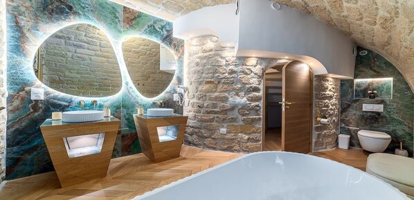 A bathroom with a stone wall, a wooden vanity, a bathtub, and a mirror with a circular frame.