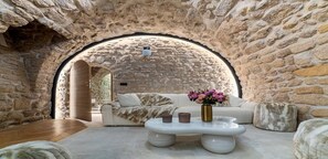 Une pièce chaleureuse avec une arche en pierre, un canapé blanc, une table basse en marbre et un vase rempli de fleurs.