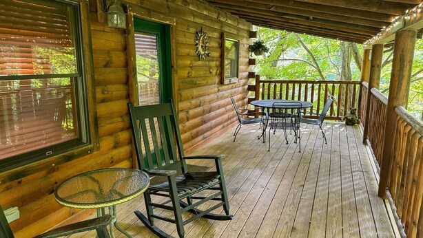 A wooden cabin with a porch featuring a rocking chair, a glass table, and a metal table with chairs.