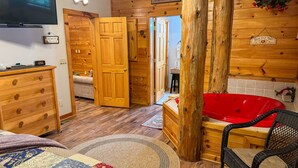 A cozy cabin interior with a wooden floor, a red hot tub, a wicker chair, and a wooden dresser.