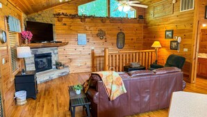 A cozy cabin interior with a fireplace, wooden walls, a leather sofa, and a dining area.