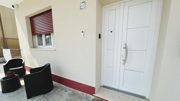 A building entrance with a double door, a small window with blinds, and two black chairs outside. - Rustico da Pina con Angolo Cottura (Castions)