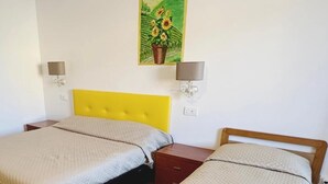 A room with two beds, each with a distinct headboard color, a wall-mounted painting of sunflowers, and bedside lamps. - Rustico da Pina con Angolo Cottura (Castions)