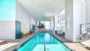 A swimming pool with a clear water surface, surrounded by a modern building with large windows and a view of other buildings.