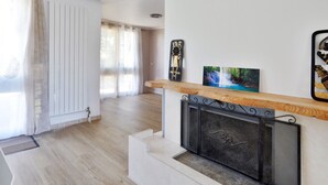 A modern living room with a fireplace, wooden flooring, and a white radiator. - Large villa for 10 people, green setting (Férolles-Attilly)
