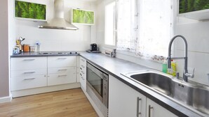 A modern kitchen with white cabinets, a stainless steel sink, and a window with a view of greenery. - Large villa for 10 people, green setting (Férolles-Attilly)