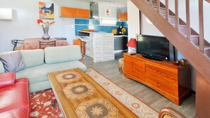 A living room with a sofa, a coffee table, a TV on a wooden cabinet, and a staircase. - Large villa for 10 people, green setting (Férolles-Attilly)