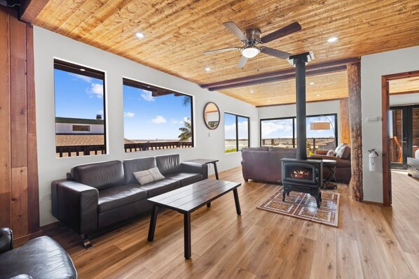 Amplia sala de estar con chimenea, sofá de cuero y ventanas grandes que ofrecen vistas del paisaje.