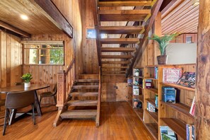 Un interior de madera con una escalera, una mesa con sillas y una estantería llena de libros.