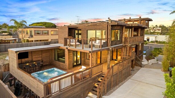 A multi-story wooden house with a hot tub, outdoor seating, and a deck.