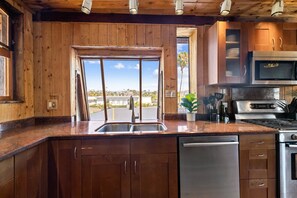 Een keuken met houten kasten, een roestvrijstalen spoelbak, een vaatwasser, een fornuis en een magnetron.