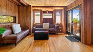 A wooden interior with a brown leather sofa, a black ottoman, and a glass door leading outside.