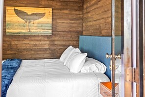 Quarto de cabana de madeira com cama, cabeceira azul e pintura de baleia na parede.