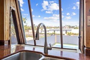 Cozinha com pia de aço inoxidável e janela com vista para um bairro residencial.