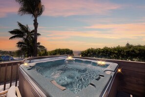 Un jacuzzi con terraza de madera y vista al atardecer.