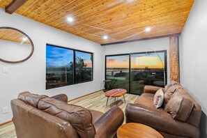 Una sala de estar moderna con sofás de cuero, un espejo redondo y ventanas amplias que ofrecen vista al atardecer.