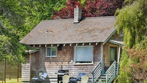 A wooden cabin with a chimney, a deck with chairs, and a small outdoor grill.