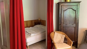 Une chambre à coucher avec un lit, une chaise en osier, une armoire en bois et des rideaux rouges.