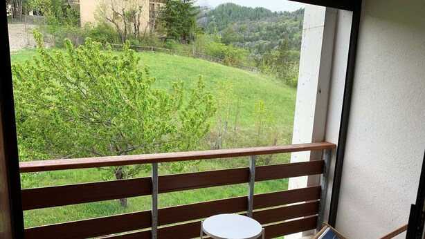 Un balcon avec une balustrade en bois, une petite table ronde et deux chaises pliantes.