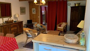 Une pièce chaleureuse avec un plafond en bois, une table à manger recouverte d’une nappe rouge, des chaises en osier, un buffet en bois et un téléviseur.