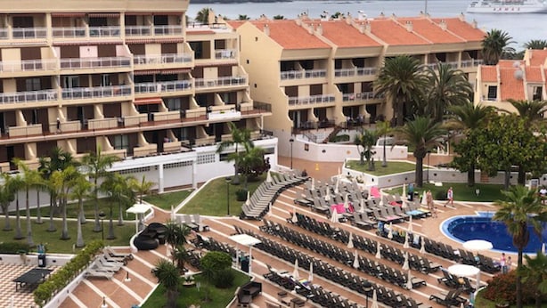 A hotel with multiple balconies, a pool area with sun loungers, and a view of the sea. - Compostela Beach Family Garden Los Cristionas (Arona)