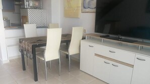A modern kitchen with a dining area, featuring a large flat-screen TV, white cabinetry, and a tiled floor. - Compostela Beach Family Garden Los Cristionas (Arona)