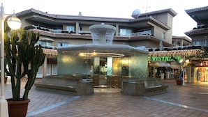 A courtyard with a central fountain, surrounded by potted plants and a building with a sign reading "VISTAS". - Compostela Beach Family Garden Los Cristionas (Arona)