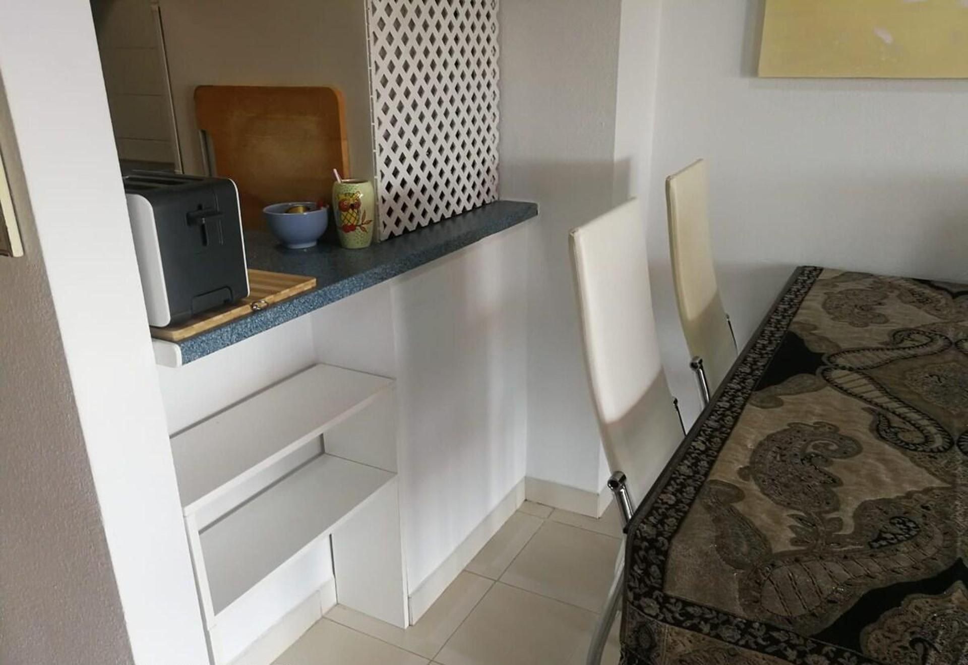 A compact kitchen with a built-in stove, a small sink, and a countertop with a toaster and a bowl.