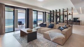 Ein modernes Wohnzimmer mit einer großen Couch, einem Couchtisch und Meerblick durch große Glasfenster.