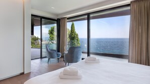 Ein modernes Hotelzimmer mit einem großen Bett, zwei Sesseln, einem kleinen Tisch und Blick aufs Meer.
