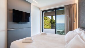 Ein modernes Hotelzimmer mit einem großen Bett, einem flachbildfernseher an der Wand und einem Balkon mit Meerblick.