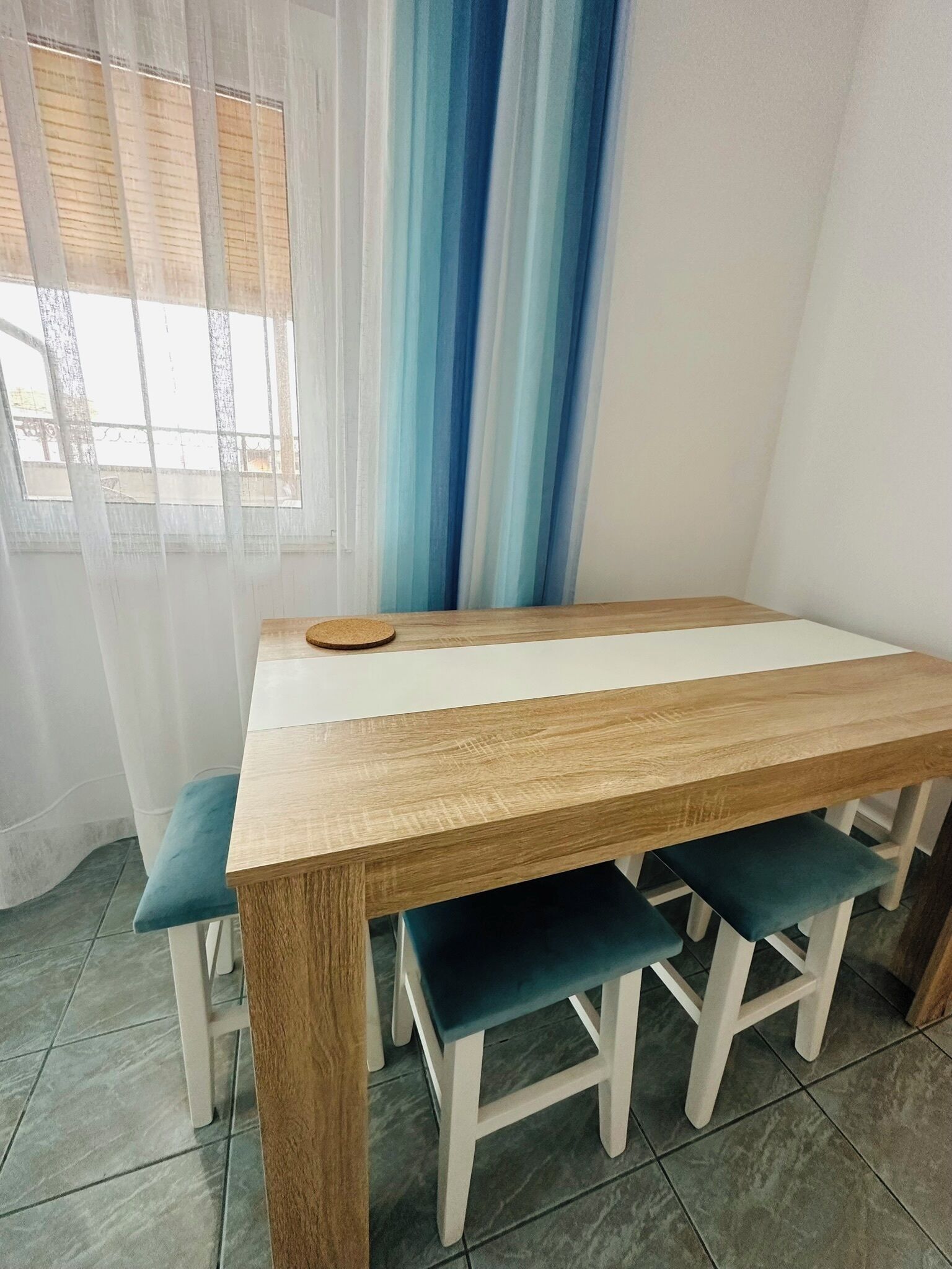 A dining area with a wooden table and matching chairs, a window with sheer curtains, and a view of the outside.