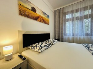 Relax in a serene space with a large bed, a painting of a wheat field, and a window with sheer curtains.