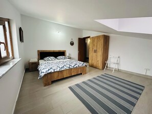 A modern bedroom with a wooden bed, a nightstand, a wardrobe, and a view of the outside through a window. - Serenity Apartments and Studios (Eforie)
