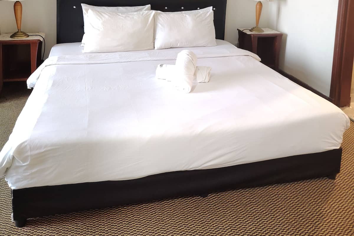 A neatly made bed with white linens, a dark headboard, and two bedside tables with lamps.